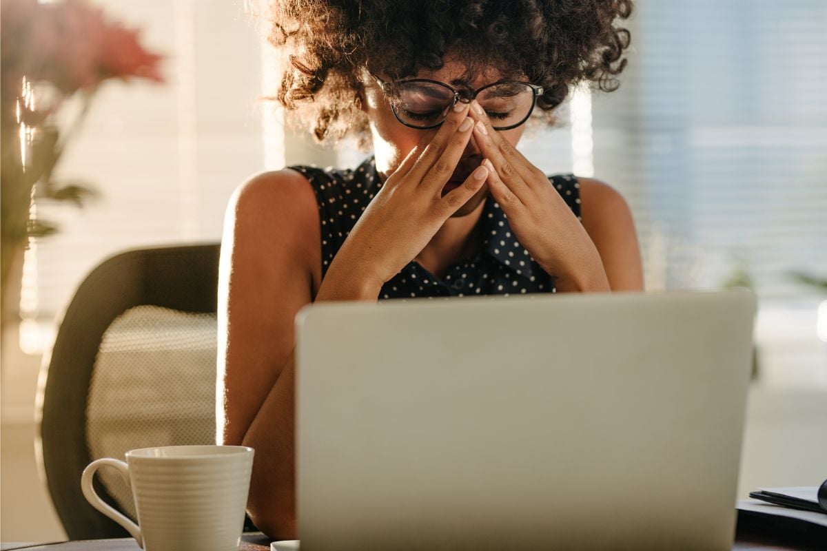 Vrouw met krullen achter laptop die door ogen wrijft