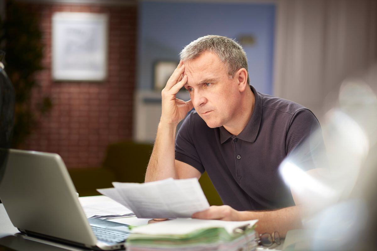 man die stressvol naar computer kijkt met stapel papieren