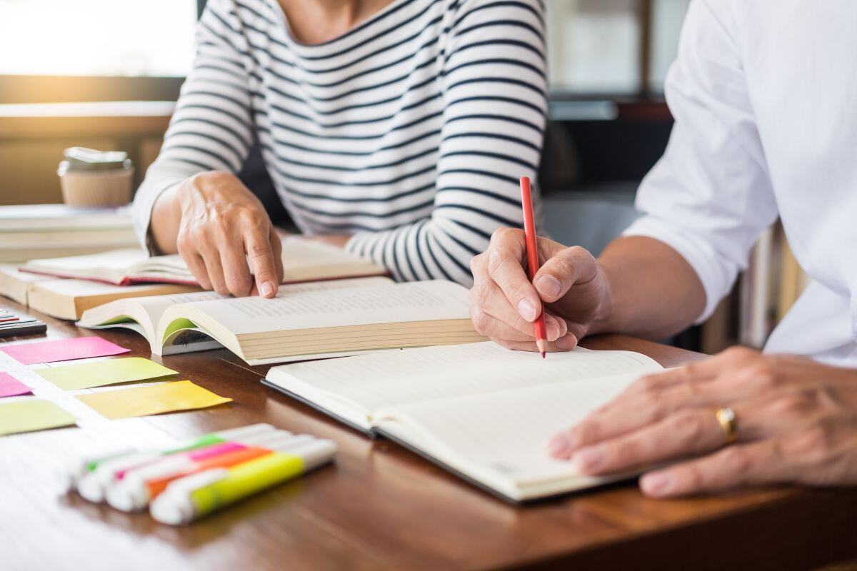 Man en vrouw waarvan je alleen de handen ziet die aan het studeren zijn met boeken en post-its