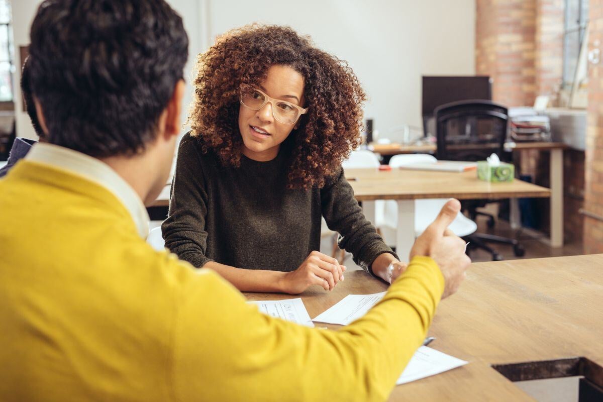 Vrouw en man aan een tafel in gesprek met papieren voor zich