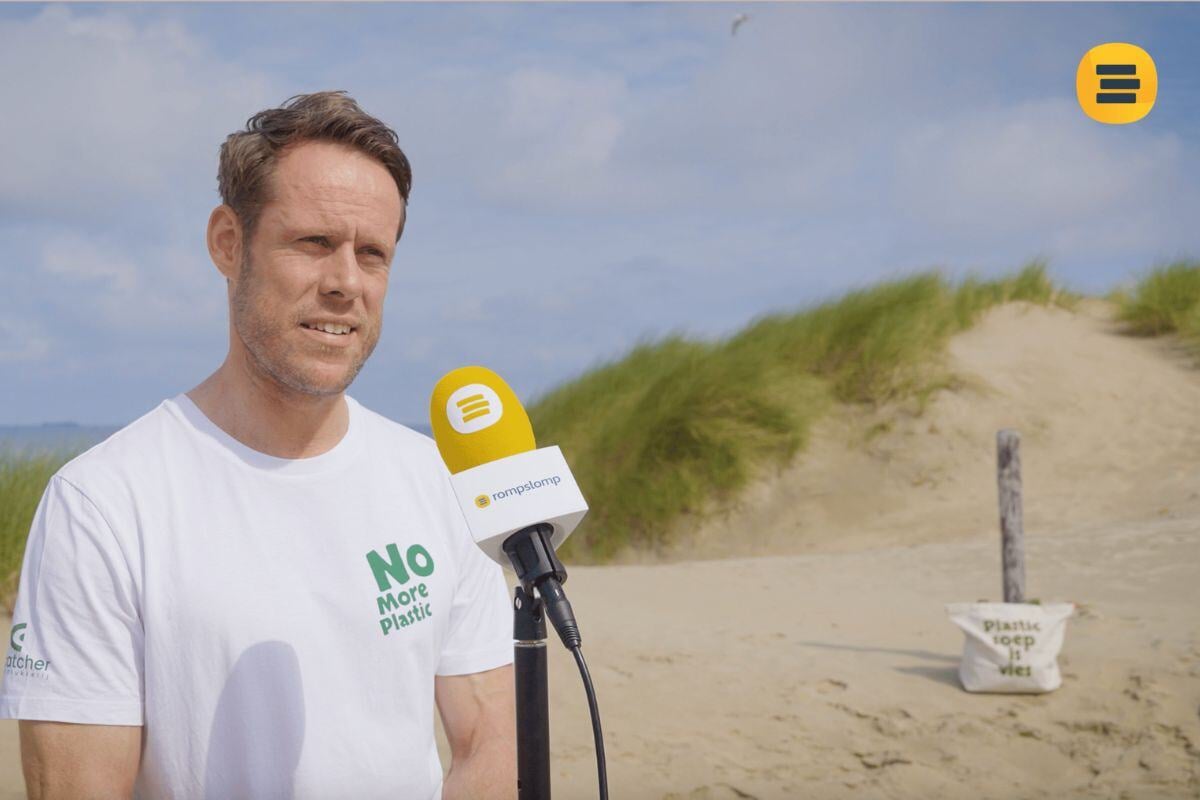 Man in de duinen met een gele microfoon voor zich met het logo van Rompslomp