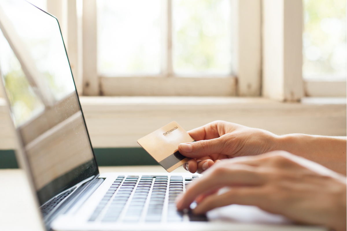 laptop met twee handen en in ee hand een bankpas