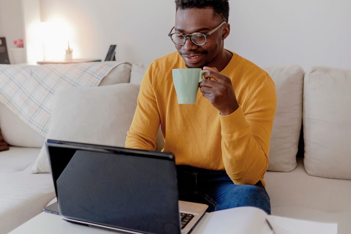 Man met koffie in hand achter een laptop en een lach op zijn gezicht